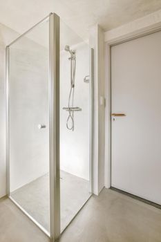 Shower faucets attached to tiled wall near glass partition and ornamental curtail in washroom at home