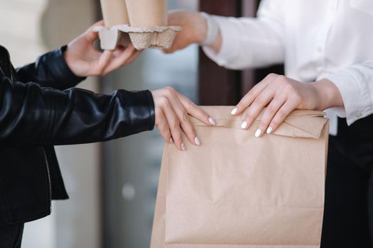 Closeup of female standing outdoors by cafe and paying with smartphone during Covid-19 pandemic. Cashier hand holding credit card reader machine while client holding phone for NFC payment. Focus on hand with package.