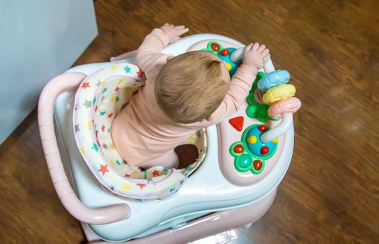 Baby is learning to walk on a walker. Selective focus. People.
