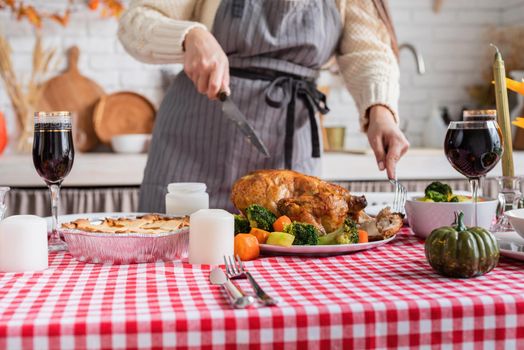 Happy Thanksgiving Day. Autumn feast. Woman celebrating holiday cooking traditional dinner at kitchen with turkey, vegetables and pumpkin pie, cutting