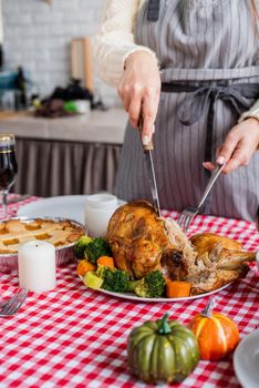 Happy Thanksgiving Day. Autumn feast. Woman celebrating holiday cooking traditional dinner at kitchen with turkey, vegetables and pumpkin pie, cutting