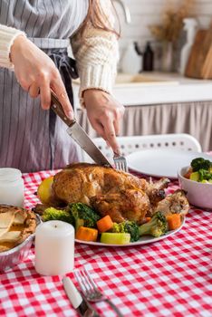 Happy Thanksgiving Day. Autumn feast. Woman celebrating holiday cooking traditional dinner at kitchen with turkey, vegetables and pumpkin pie, cutting