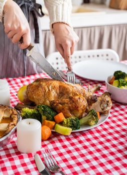 Happy Thanksgiving Day. Autumn feast. Woman celebrating holiday cooking traditional dinner at kitchen with turkey, vegetables and pumpkin pie, cutting