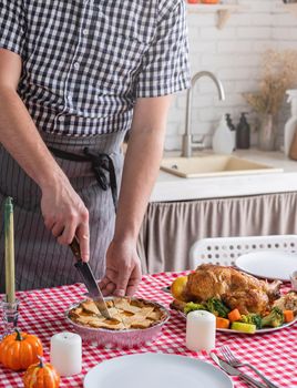 Happy Thanksgiving Day. Autumn feast. man celebrating holiday cooking traditional dinner at kitchen with turkey, vegetables and pumpkin pie, cutting pie