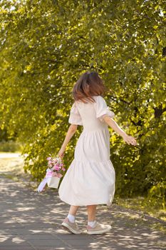 A beautiful bouquet of flowers in a box in the hands of a beautiful girl who walks along the street on a sunny day. Girl in a dress, glasses and sneakers. Focus on the background of flowers.