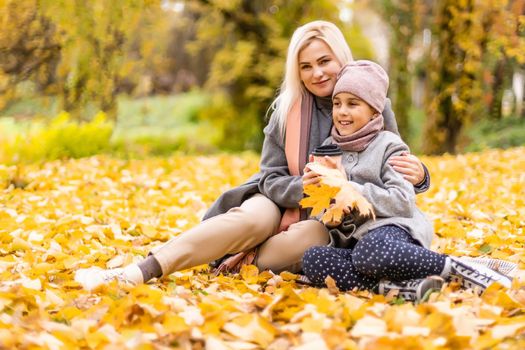 Mother and daughter having fun in the autumn park among the falling leaves