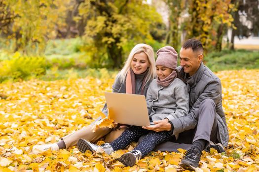 happy family with little daughter smiling happily looking at laptop screen walking in park.
