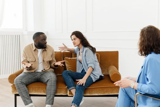 Stressed unhappy millennial Caucasian and African American couple have relationship problems. Diverse couple fighting while visiting professional psychologist for help, breakup prevention concept