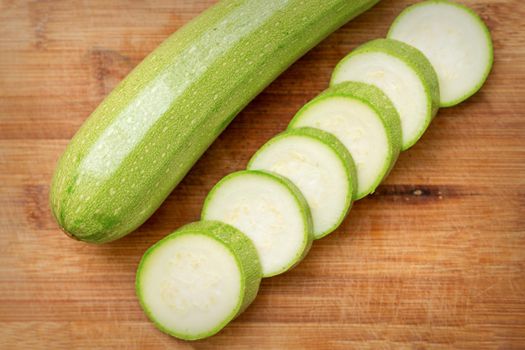 Slices of courgettes on wooden chopping board. Fresh green zucchini whole and cut into slices on cutting board