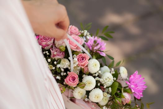 A beautiful bouquet of flowers in a box in the hands of a beautiful girl who walks along the street on a sunny day. Girl in a dress, glasses and sneakers. Focus on the background of flowers.