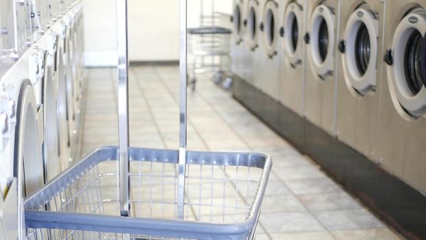 Row of washing and drying machines, public coin laundry in California, USA. Drums of washers and dryers in self-service laundromat or commercial laundrette. Automatic launderette in United States.