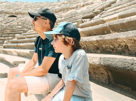 Young father dad and his school boy kid son tourists visiting ancient antique coliseum amphitheater ruins in hot summer day.