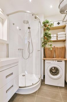 Shower box in modern bathroomShower cubicle, washing machine under shelves with towels and wicker baskets in a small modern bathroom