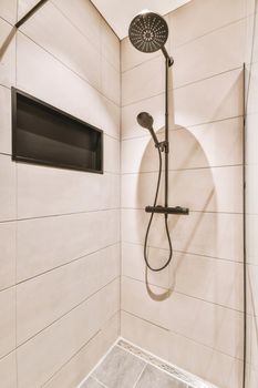 Shower faucets attached to tiled wall near glass partition and ornamental curtail in washroom at home