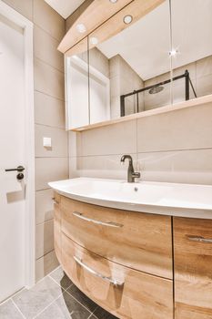 Cupboard with sink and mirror attached to tiled wall near door and drying rack in modern restroom