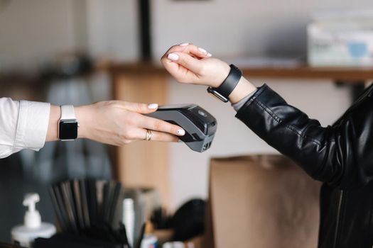 Female customer making wireless or contactless payment using smartwatch. Closeup of hands during payment. Store worker accepting payment over nfc technology.