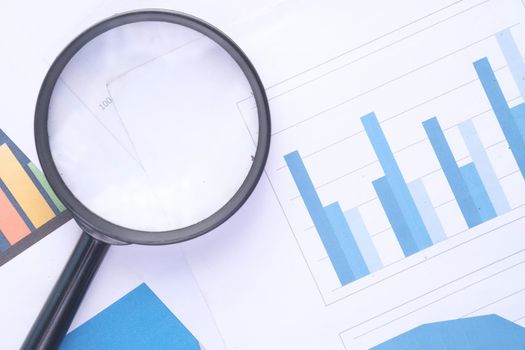 financial graph, magnifying glass on table .