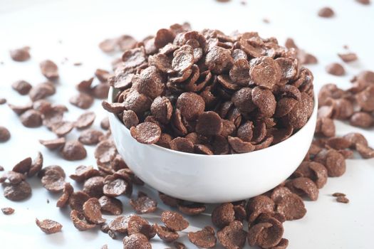 close up of chocolate corn flakes in a bowl on white .