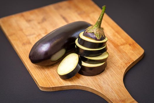 Fresh sliced eggplant on wooden cutting board isolated on black. Cooking ingredients