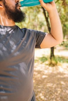 cropped shot of a young fitness man drinking water from a bottle after a sports workout to refresh herself. boy practising sport outdoors. health and wellness lifestyle.outdoor public park, natural sunlight.. vertical