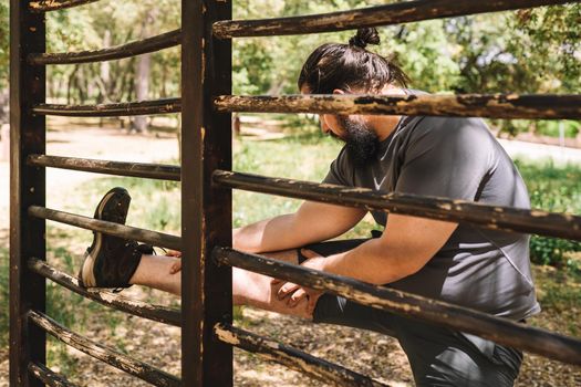 young man practising leg stretching exercises leaning on a trellis. athlete preparing for a championship. health and wellness lifestyle. Natural sunlight, background of natural vegetation, forest, sportswear.