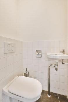 Wall hung toilet and small sink in corner in lavatory room with beige tile