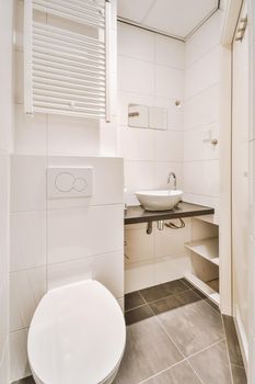 Modern flush toilet and ceramic sink installed on white tiled walls near mirror and towel in small restroom at home