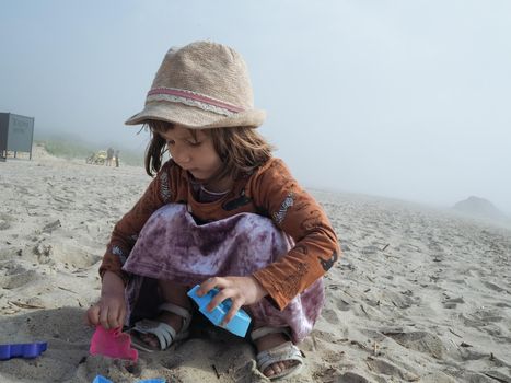 Girl playing sand toys at the beach. Foggy day. Copyspace
