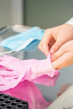 Nurse's hands putting on pink sterilized protective gloves in the laboratory