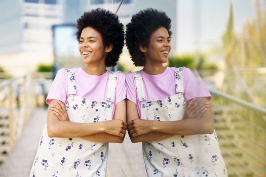 Cheerful black woman in casual clothes laughing in the street. Happy young femeale, afro hair, in urban background.