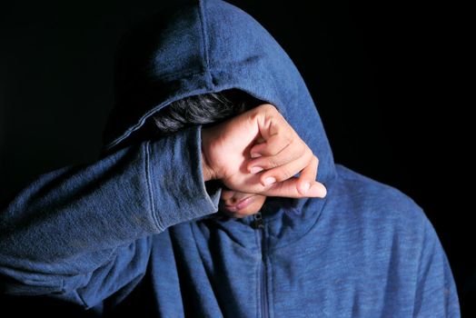 sad man in hood cover face with hands isolated in black