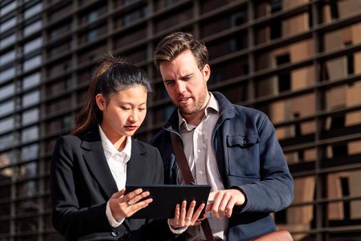 young entrepreneur woman showing her tablet to a businessman next to an office building in the financial district, concept of entrepreneurship and business