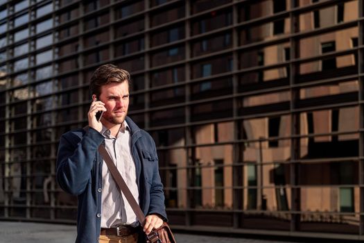 young businessman walking by the offices in the financial district talking on the telephone, concept of entrepreneurship and business, copy space for text