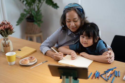 Smiling senior grandma and cute little kid granddaughter watching cartoons on laptop together, happy older grandmother grawing and painting