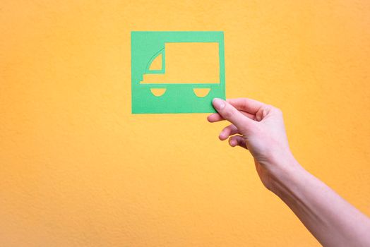 Hand holds green logistics symbol on yellow background.