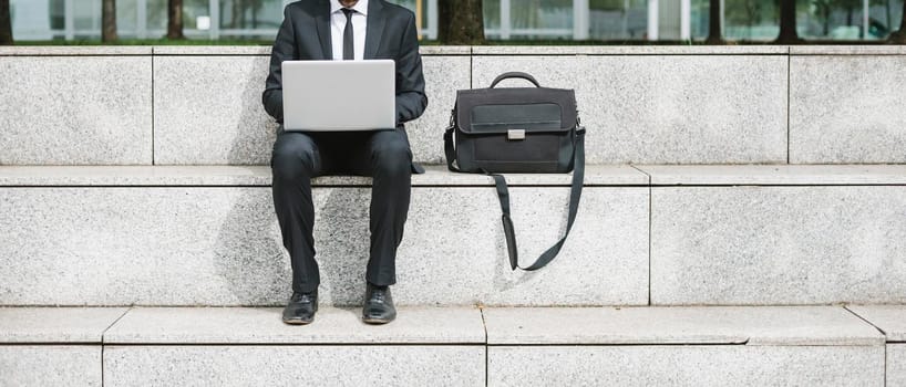 Business sitting in the city working at laptop wearing suit