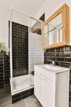 Bathtub with glass shower placed in corner near sink and mirror in small light bathroom with whiteand black tile walls