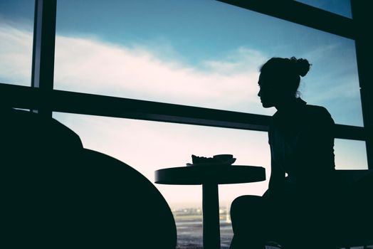 Woman waiting at airport lounge against window sitting at table.