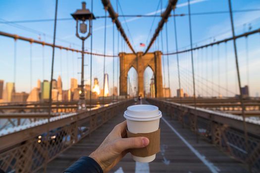 Man holding coffee cup in New York City Brooklyn bridge.