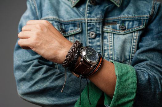 The man in jean jacket wearing bracelets and wristwatch, casual style of men accessories. Shallow depth of field.