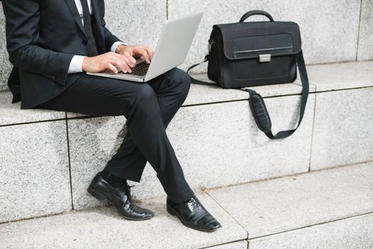 Business sitting in the city working at laptop wearing suit