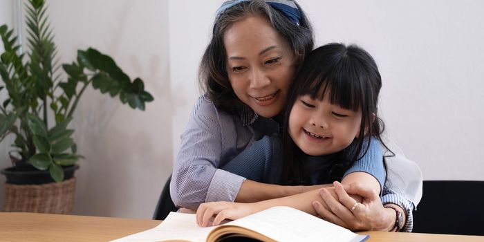 happy asian family grandmother reading to granddaughter child book at home.