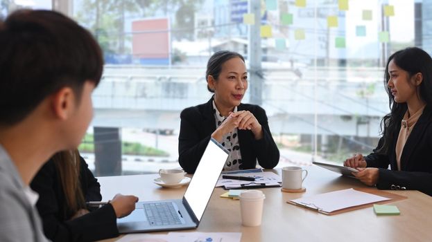 Smiling young female team leader coach discussing market research results to diverse business people at briefing.