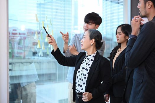 Diverse business people brainstorming and sharing creative ideas throughs colorful sticky notes on glass window.