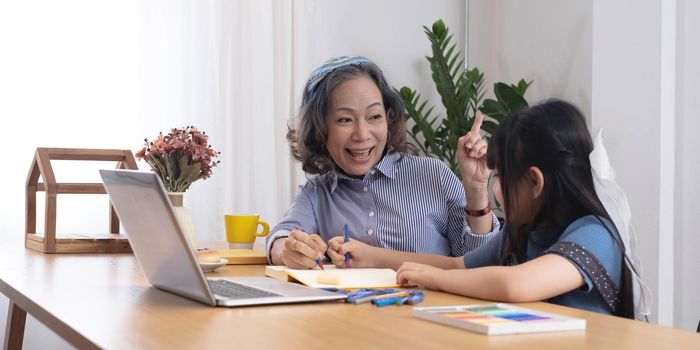 Asian grandmather teach granddaughter drawing and doing homework at home.