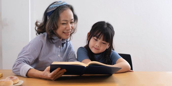 happy asian family grandmother reading to granddaughter child book at home