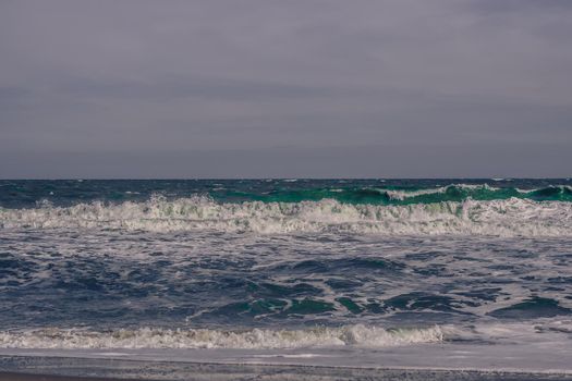 Ocean storm waves dramatically crashing splashing. Sky horizon line. Sea water edge, nature front view marine wallpaper, design. Bad weather cloudy overcast. Dark green turquoise blue tone pale matte.