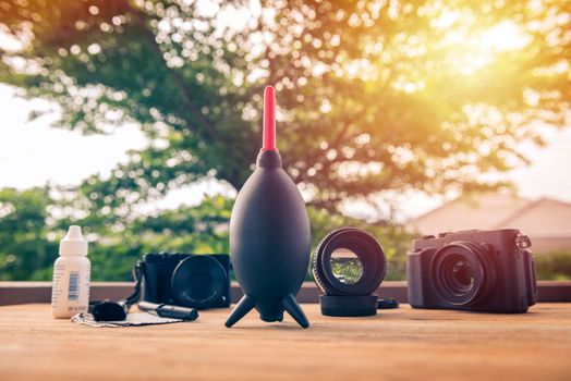 black mirrorless camera with lens attached with camera cleaning kits in background on wooden desk. Camera and lens care.