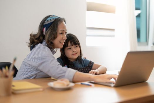 Older woman grandma and little girl grandkid with homework remote study. Attentive mature old female tutor give private lesson to small child pupil.