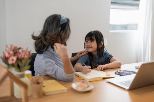 Older woman grandma and little girl grandkid with homework remote study. Attentive mature old female tutor give private lesson to small child pupil.